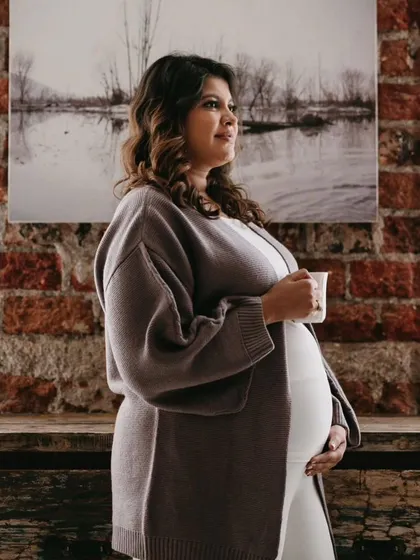 A beautiful candid moment. The mom-to-be looks radiant and serene, with a natural makeup look that complements the cozy, indoor setting.