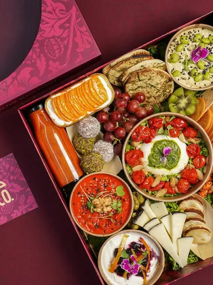 A closer look at a beautifully arranged grazing box. This one features a stunning burrata with pesto and cherry tomatoes, edamame hummus, assorted cheeses, fresh grapes, and energy bites, perfect for a sophisticated palate.