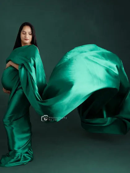 An artistic shot using a flowing green satin fabric to create a dynamic and abstract shape around the mom-to-be.