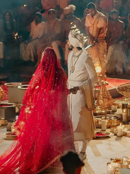 The couple is surrounded by guests and traditional lamp bearers during their Varmala ceremony.