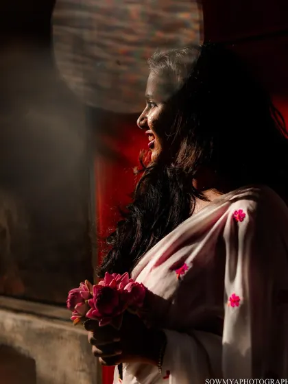 A bride-to-be smiles, holding a bouquet of lotuses, with a dramatic play of light and shadow creating an artistic and soulful portrait.