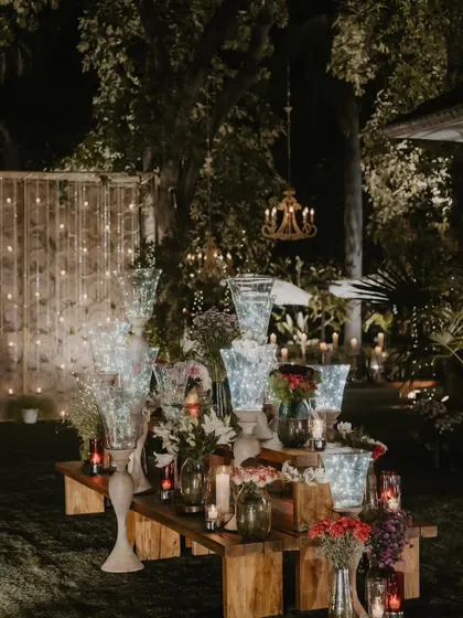 A rustic wooden table adorned with an array of glass vases, fairy lights, and flowers.