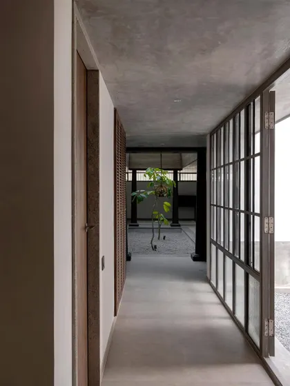 A well-lit linear gallery with a polished concrete floor connects the two wings of the house. One side opens to an outdoor court, ensuring the corridor is bright and feels connected to the outdoors.