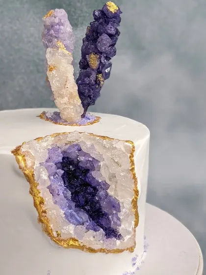 A different angle of the purple geode cake, shot against a lighter background. This view highlights the sparkle of the homemade rock crystals and the clean, sharp edges of the whipped cream frosting.