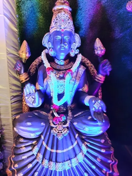 A statue of Goddess Lakshmi adorned with a simple garland and lit with blue light for a dramatic effect.