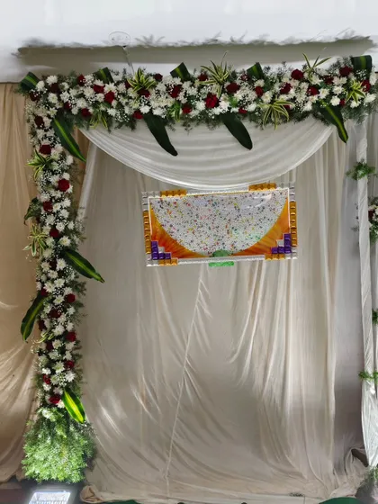 A simple and elegant naming ceremony backdrop. The decor uses a white curtain framed by fresh flower arrangements in white and red.