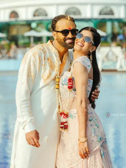 A happy and relaxed portrait of the couple after their Haldi ceremony, embracing by the pool with sunglasses on.