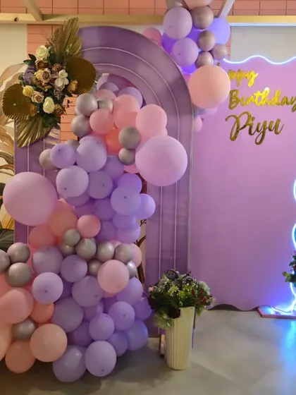 A stylish photo corner with a lavender arched backdrop and a custom neon sign. The cascading balloon arrangement in shades of purple, pink, and silver adds a touch of modern elegance.