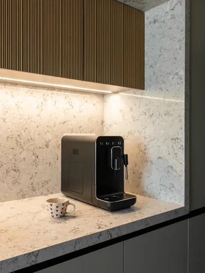 A close-up of fluted wood cabinets above a coffee station. The under-cabinet lighting highlights the texture, adding depth and creating a cozy, inviting corner for your morning brew.
