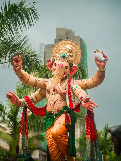 A full view of a magnificent Ganesh idol during the Aagman Sohala, or welcoming procession. The shot is taken from a low angle to emphasize its grand size against the Mumbai skyline.