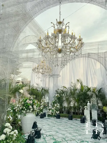 Inside the wire-mesh chapel, magnificent crystal chandeliers hang above a floor of hand-painted tiles and are surrounded by potted palms and white floral arrangements, blending classic luxury with a botanical garden feel.