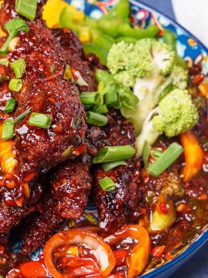 A close-up of our Safeer Chongqing Chicken, a spicy and flavorful dish featuring deep-fried chicken tossed with a generous amount of chili, Sichuan peppercorns, and fresh vegetables like broccoli and bell peppers.