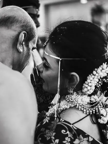 A black and white photo capturing an intimate conversation between the bride and her father amidst the wedding rituals.