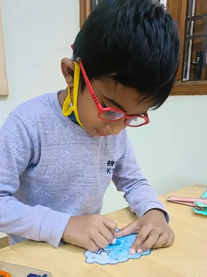 A young boy with glasses carefully colors his artwork, showing great concentration.