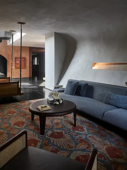 A serene living area in the Baid Residence, featuring a curved sofa that follows the architectural lines of the space. The room is designed as a quiet retreat, with a traditional swing and a curated selection of art.
