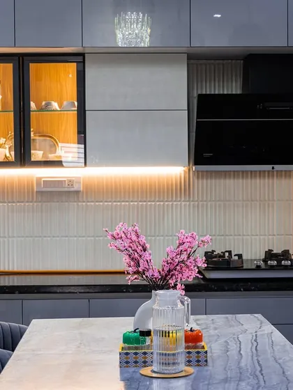A view of the kitchen's cooking area, with a black chimney hood and a glass-front cabinet for display. The under-cabinet lighting creates a warm and inviting glow.