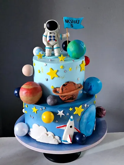 An out-of-this-world space-themed cake for an 8th birthday. This multi-tiered cake is decorated with hand-painted planets, edible stars, a rocket ship, and a detailed astronaut figurine planting a personalized flag.