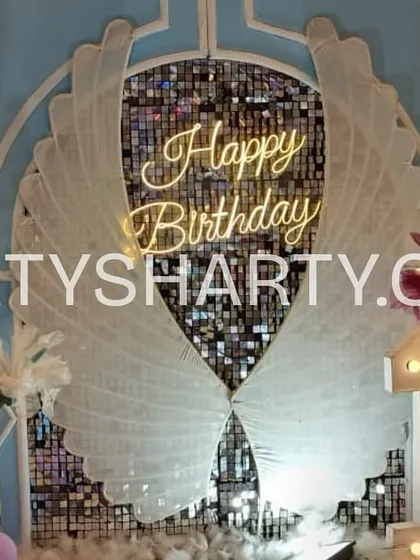 A beautiful Frozen-themed photo backdrop with angel wings, a 'Happy Birthday' neon sign, and a floor covered in faux snow.