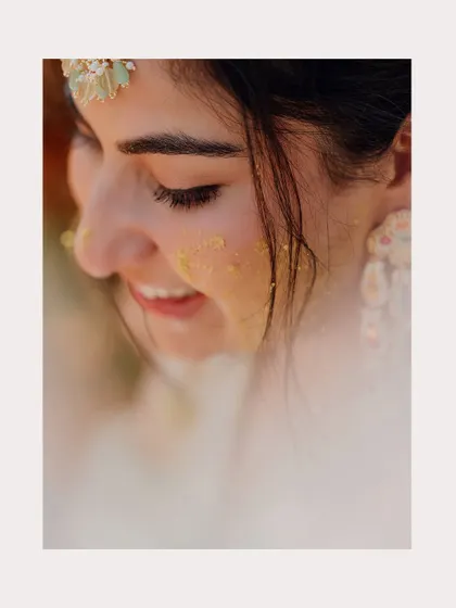 A soft, beautiful close-up of the bride with a touch of Haldi on her cheek, smiling gently.