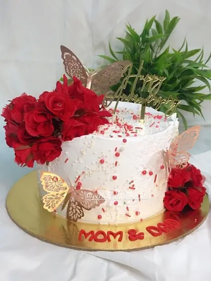 A timeless combination of red and white for a pretty floral anniversary cake. This design uses whipped cream frosting, red roses, and delicate gold butterflies for a classic and romantic feel.