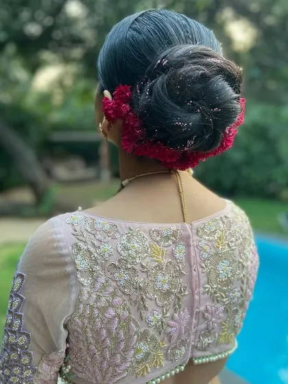 A high bridal bun wrapped in vibrant red coxcomb flowers. The unique texture of these flowers adds a rich, velvety look to the hairstyle.