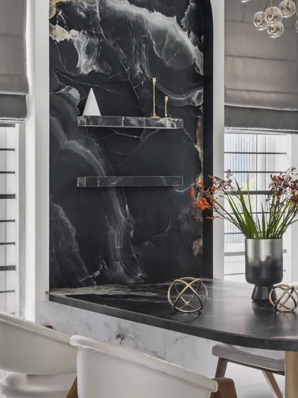 A detail shot of the custom-built dining table and its dramatic black tile backdrop. The dark, monolithic feature provides a stunning contrast in the all-white living space, framed by large windows with custom blinds.