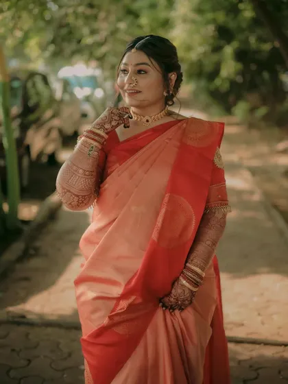 A beautiful solo portrait of the bride in a lovely peach and red saree, captured in soft, natural light.