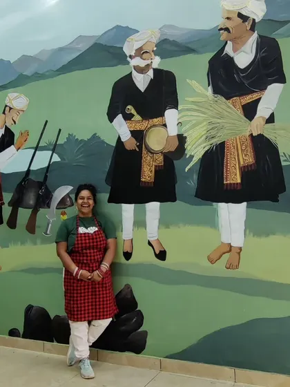 My painting partner posing with her section of the Coorg mural, which depicts the men's celebration during the Kailpodh festival.