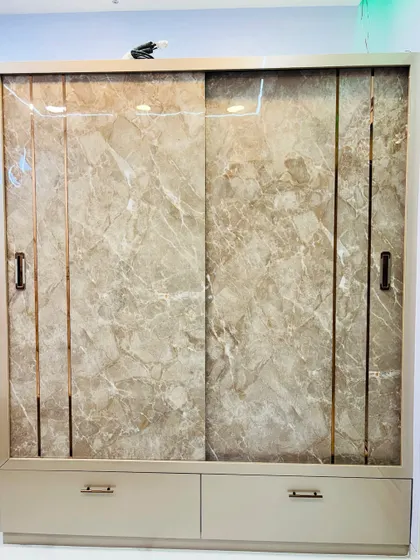 A luxurious sliding wardrobe with a beige marble-finish laminate and slim gold inlays. The drawers at the bottom provide easy access to smaller items.