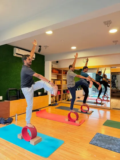 Men in our class use yoga wheels to challenge their balance and strength in a standing leg-raise pose. Yoga is for every body.