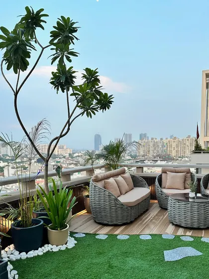 Another perspective of the rooftop terrace, showing the complete seating arrangement. The combination of natural wood, artificial grass, and curated plants creates a balanced and inviting outdoor lounge.