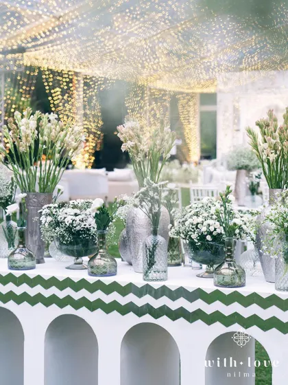 A bar setup with an assortment of white flowers under the fairy-lit tent. The design ensures that every corner of the event is visually stunning.