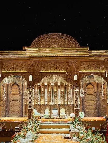 A wide shot of the magnificent South Indian wedding mandap, showcasing its grand scale and the beautiful lighting that highlights its intricate details.