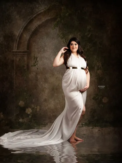 A classic fine art portrait against a dark, textured backdrop. The simple white gown and the water reflection effect create a moody, elegant, and timeless image.