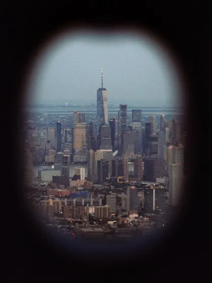 A voyeuristic view of the downtown Manhattan skyline, seen through a binocular viewer. This framing adds a sense of distance and observation.