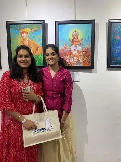 Two students posing with their artwork and an NS Kumbar Art tote bag at the exhibition.