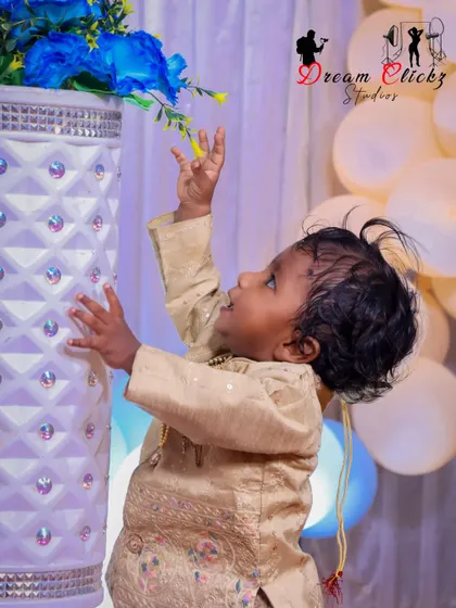 An adorable action shot from a birthday celebration. The baby reaches for a flower in a vase, and the photo freezes a moment of innocent curiosity and discovery.