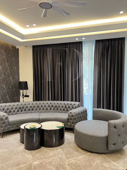 Timeless elegance meets modern comfort. This living space features a classic tufted Chesterfield sofa and a curved accent chair, set against a backdrop of dramatic marble walls and sophisticated cove lighting, creating a warm and inviting atmosphere.