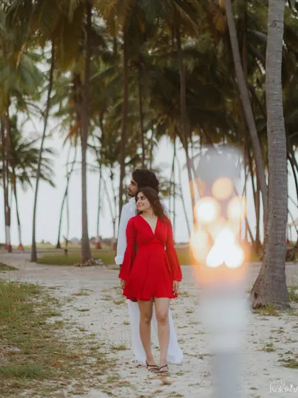 A creative portrait using foreground elements to frame the couple against a backdrop of palm trees, adding depth and an artistic touch to this beach pre-wedding shot.