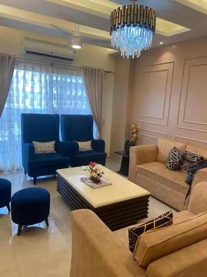 A cozy living room from a completed project, featuring high-back blue armchairs and a comfortable beige sofa. The elegant chandelier and wall molding add a touch of classic charm.