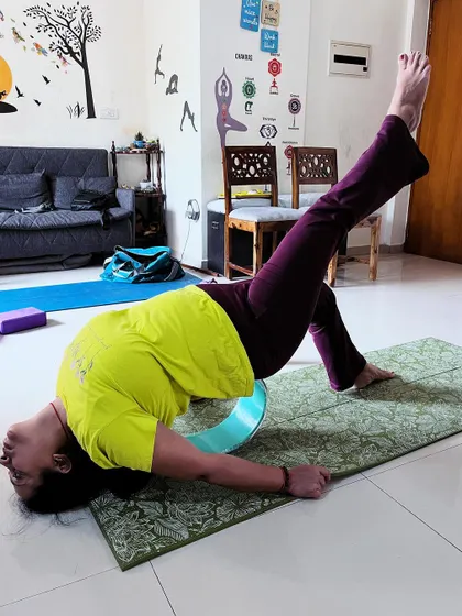 A client uses a yoga wheel for a supported backbend with a leg lift, a challenging variation that builds strength and flexibility simultaneously.