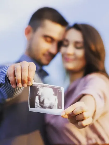 A classic maternity announcement photo. This couple shares their joy by holding up their baby's first picture, the ultrasound scan, in a beautifully composed outdoor shot.