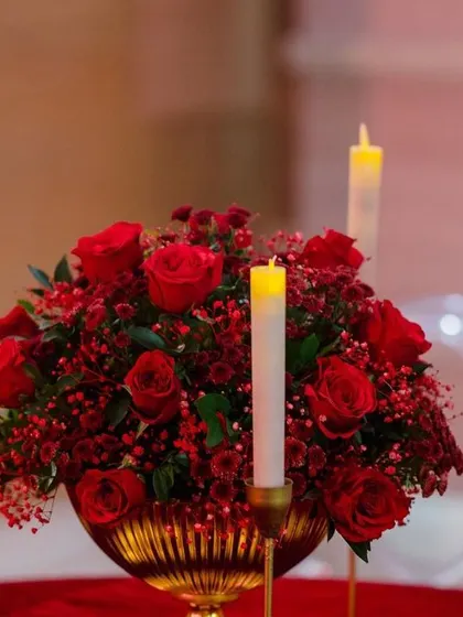 A luxurious centerpiece featuring a bouquet of deep red roses in a golden vase. This classic and elegant detail was part of a glamorous red-themed reception.