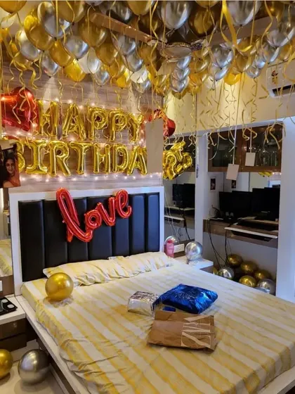 A lavish gold and silver balloon decoration for a surprise birthday. The entire ceiling is covered with balloons, creating a festive canopy above the bed, ready for celebration.