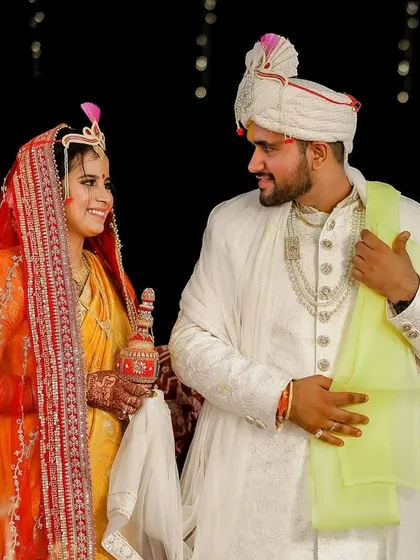 The couple shares a look during a traditional ritual, the bride holding a ceremonial pot. This image captures the cultural richness and shared joy of their wedding ceremony.