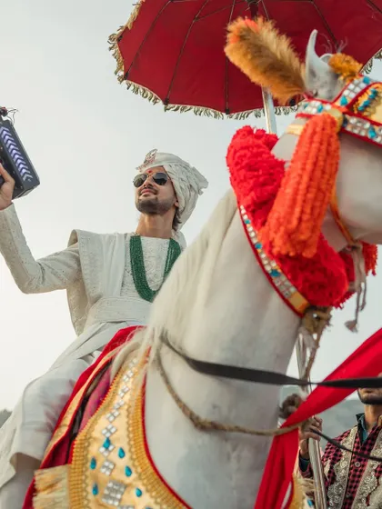 The groom makes a grand entrance on a majestic horse, holding a CO2 gun, blending tradition with modern-day swag.