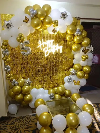 A classic and elegant theme for a 5th birthday using a gold and white color palette. This circular balloon arch with a neon sign and a number '5' foil balloon creates a stunning centerpiece for the celebration.