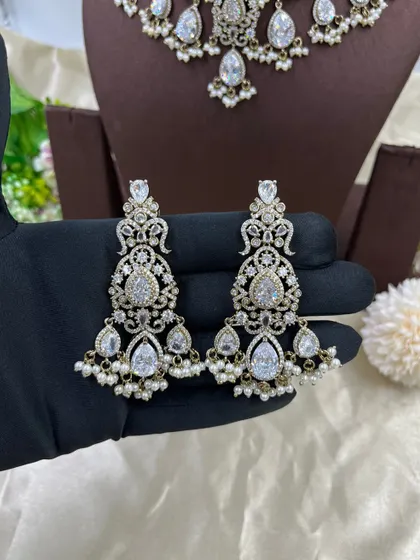 A close-up of our all-white AD and pearl earrings. The intricate design and dangling pearls make these a sophisticated choice for elegant evening wear.