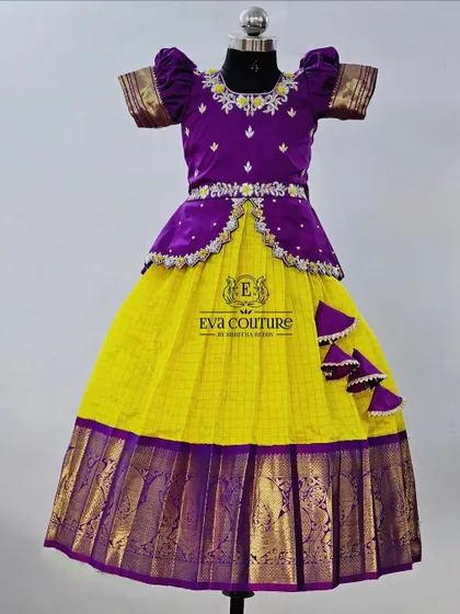 A vibrant yellow and purple pattu pavadai. The purple peplum top has delicate silver embroidery, which complements the yellow checked skirt with its purple zari border.