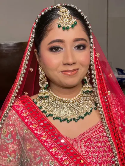 A classic bridal look featuring soft brown and gold eyeshadow. The makeup is elegant and understated, allowing her beautiful green jewelry to stand out.